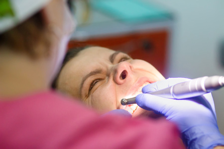 Dentist brushing his teeth to the patient. Dentist is drilling teeth to a young woman