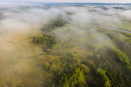 Foggy summer morning nature aerial view. Mist over green meadow with river. Misty nature landscape from aboveの写真素材