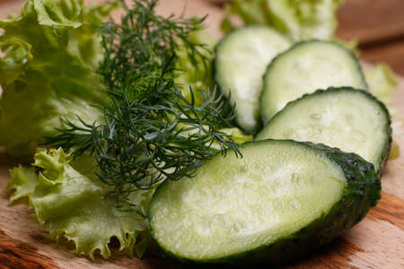 Cucumber, lettuce and dill lie on the kitchen wooden board. Top view close-upの写真素材