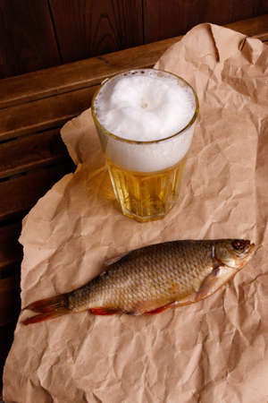 Close-up dried fish, a glass of beer on a dark wooden background.