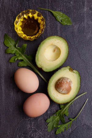 On a dark table are eggs, avocados, olive oil and greens. View from aboveの写真素材
