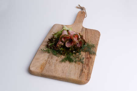meat balyk with fresh green salad and dill on a wooden board and white backgroundの写真素材