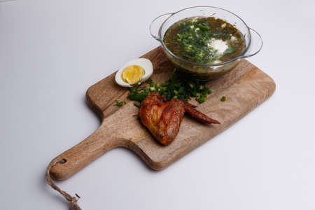 soup, chicken wing, egg and greens on a wooden board on a white backgroundの写真素材