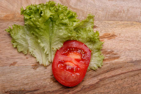Sliced tomato and lettuce leaves lie on a wooden kitchen board. Close-up