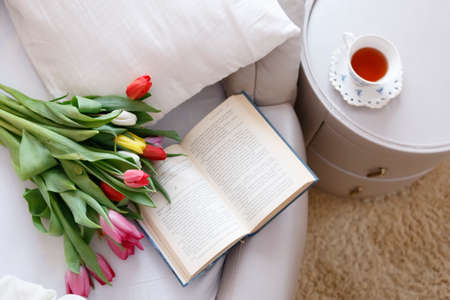 bouquet of tulips, a book and tea on the background of bed linen