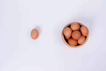 Yellow, beige and white chicken eggs in a wooden plate, one egg next to the plate. White background. Isolateのeditorial素材