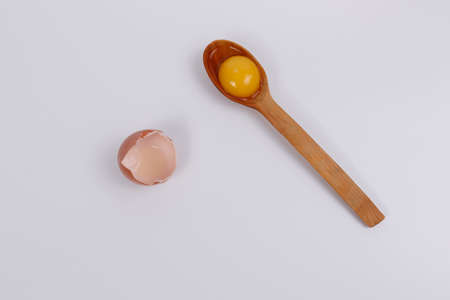 Egg yolk in a wooden spoon, next to the eggshell. White background. Isolateのeditorial素材