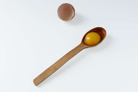 Egg yolk in a wooden spoon, next to the eggshell. White background. Isolateのeditorial素材