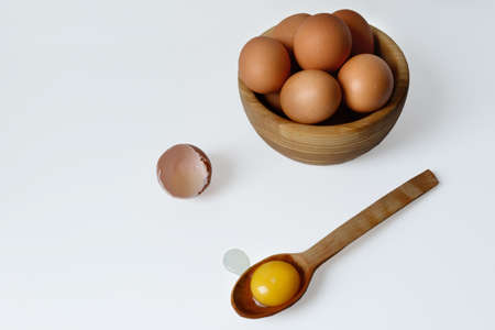 Chicken eggs in a wooden plate, next to a spoon with egg yolk and chicken shell. White background. Isolateのeditorial素材