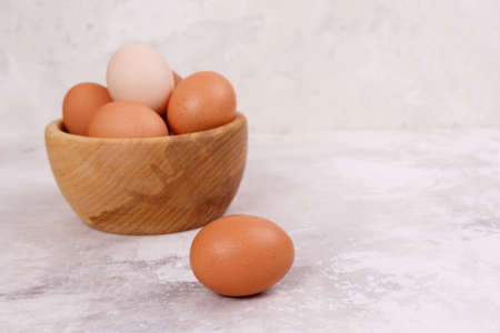 Chicken egg in the foreground. In the background eggs in a wooden plate, blurred background. Close-up. Side viewの写真素材