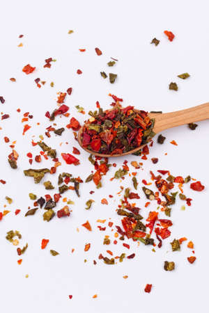 Flakes of red and green pepper in a wooden spoon on a white background. Isolate