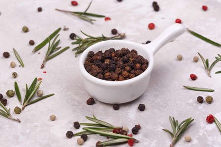 Black pepper inside a white dish. Next to the dish is rosemary leaves. Close-upの写真素材