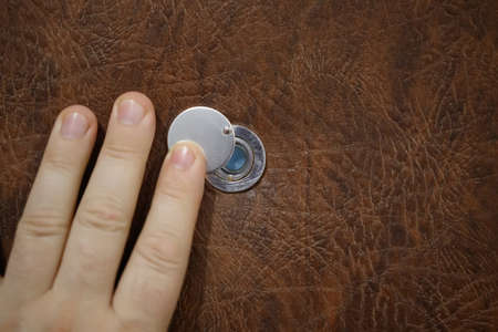 The male hand opens the peephole. Brown door. Close-upの写真素材