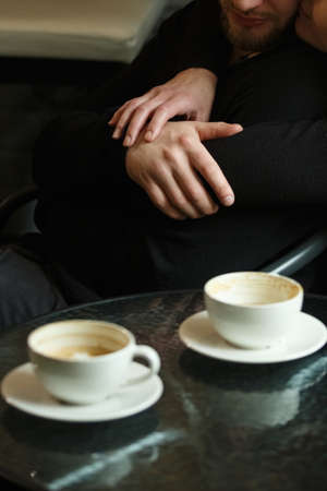 Hands of a man and woman close-up in sharpness, outside the sharpness of coffee in a cup