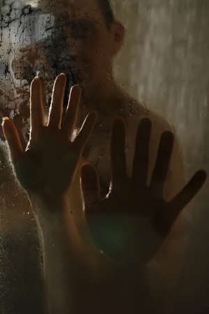 Hands of man and woman on wet glass in the shower. Close-up.