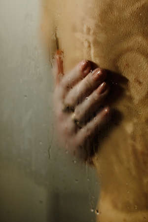 A woman hugs a man in the shower. Woman's hand on the manâs back. Behind the misted glassの写真素材
