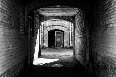 Arched passage into the courtyard of an old house. In the background there is an exit from the yard. Black and white photographyの写真素材