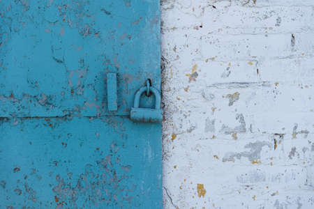 The blue door in the white wall is closed with a blue metallic lock. The picture is divided into two parts: blue and whiteの写真素材