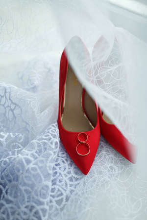 Wedding rings of the bride and groom lie on red shoes.の写真素材
