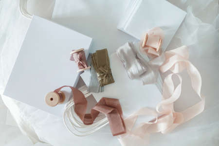 White gift box tied with a cream-colored decorative ribbon on a beige fabric background.の写真素材