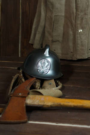 Fire helmet, ax and belt lie on wooden boards. In the background old firefighters clothesの写真素材