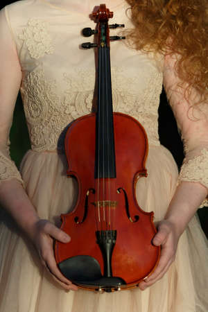 The violin is in the hands of a girl dressed in a cream dress. Violin and hands closeupの写真素材