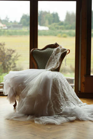 The wedding dress lies on the armchair, in the background a large windowの写真素材