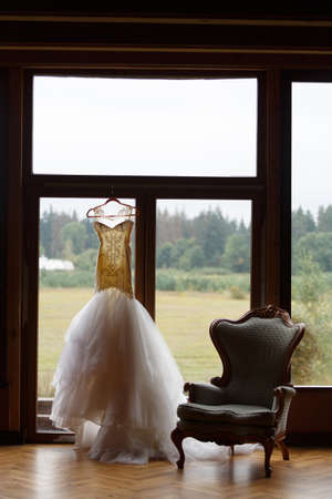 The wedding dress is hanging on the window, next to it is a chair. Outside the forestの写真素材