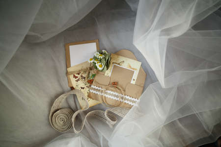 Wedding accessories: camomile buttonhole, envelope, invitation and ribbons lie on the fabricの写真素材