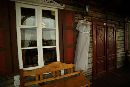 Wedding dress hanging on a lantern, between the window and the door. There is a bench nearbyの写真素材