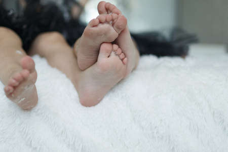 Feet of two children in feathers close-up on a white coverletの写真素材