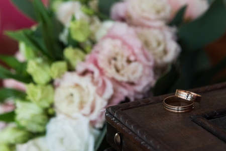 Wedding rings on a wooden frame. Near the bride's bouquet - blurred backgroundの写真素材