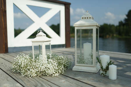 Wedding accessories: white lanterns with candles, decorated with flowers. On the pier by the lakeの写真素材
