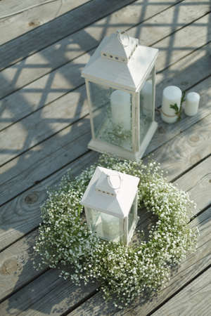 Wedding accessories: white lanterns with candles, decorated with flowers. On a wooden pierの写真素材
