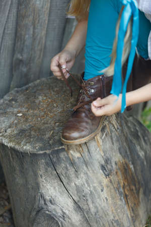 The child put his foot on a tree stump and ties a lace on shoesの写真素材