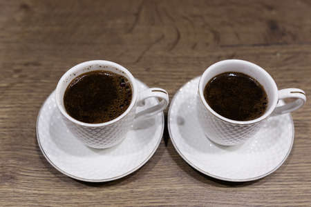 Two white cups with coffee on the table. Close-up