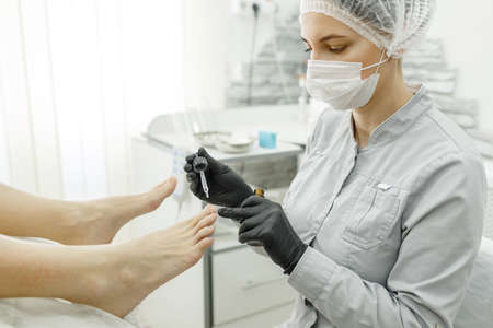 Therapeutic pedicure. The pedicure master applies a softening oil or a medicinal product in a pipette to the nailsの写真素材
