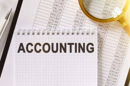 On the table are financial reports, a pen, a magnifying glass and a notebook with the inscription - ACCOUNTING. Americans with Disabilities Act. Business and finance concept.の写真素材