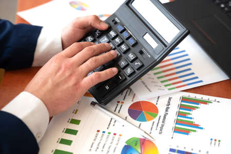 Male hand with a calculator and pen, business graph and chart. Financial conceptの写真素材