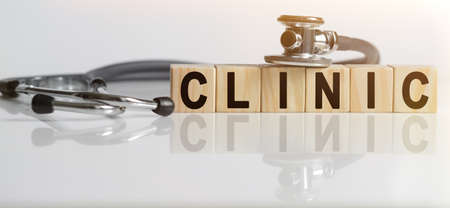CLINIC the word on wooden cubes, cubes stand on a reflective white surface, on cubes - a stethoscope. Medicine conceptの写真素材