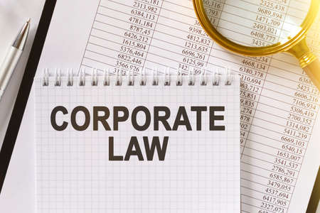 On the table are financial reports, a pen, a magnifying glass and a notebook with the inscription - CORPORATE LAW. Business and finance concept.の写真素材