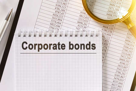 On the table are financial reports, a pen, a magnifying glass and a notebook with the inscription - Corporate bonds. Business and finance concept.の写真素材