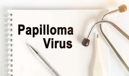 On the table are a stethoscope, a thermometer, a pen and a notebook with the inscription -Papilloma Virus. The concept of medicine.の写真素材