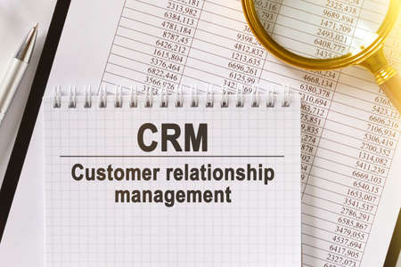 On the table are financial reports, a pen, a magnifying glass and a notebook with the inscription - CRM. Customer Relationship Management. Business and finance concept.の写真素材