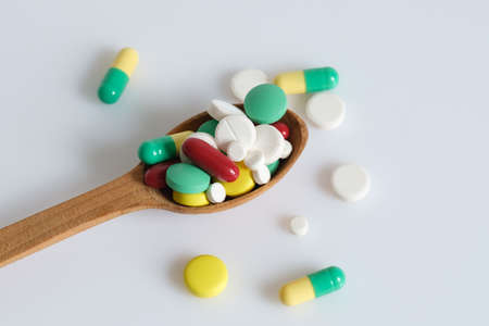 Top view of assorted pharmaceutical medicine pills, tablets and capsules on wooden spoon. Isolated on white background.の写真素材