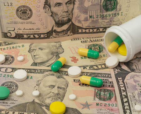 Healthcare savings and expencive medicine concept. Pills scattered over dollar banknotes. Bottle of pills and moneyの写真素材