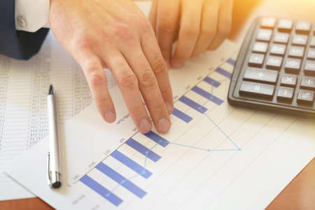 Male hand with a calculator and pen, business graph and chart. Financial conceptの写真素材