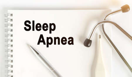 On the table are a stethoscope, a thermometer, a pen and a notebook with the inscription -Sleep Apnea. The concept of medicine.の写真素材