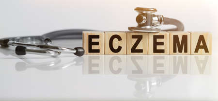 ECZEMA the word on wooden cubes, cubes stand on a reflective white surface, on cubes - a stethoscope. Medicine conceptの写真素材
