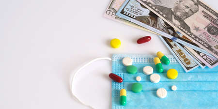 Dollars in a medical mask, surrounded by drugs and pills. The concept of medecine. Shot from above on a white background.の写真素材
